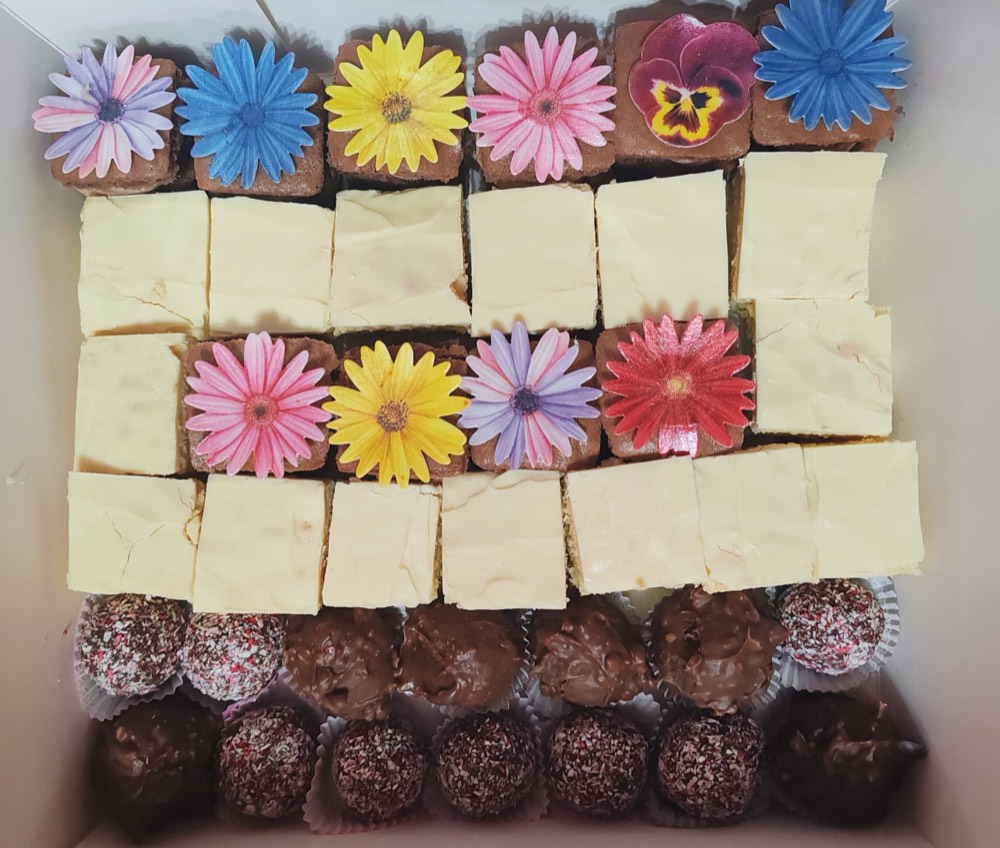 Platou cu cuburi cu cremă de cacao decorate cu flori din vafă, trufe și prăjituri cu glazură albă