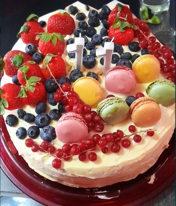 Tort aniversar cu cremă de brânză, căpșuni, afine, coacăze și macarons pastel, păstrat la rece până la eveniment